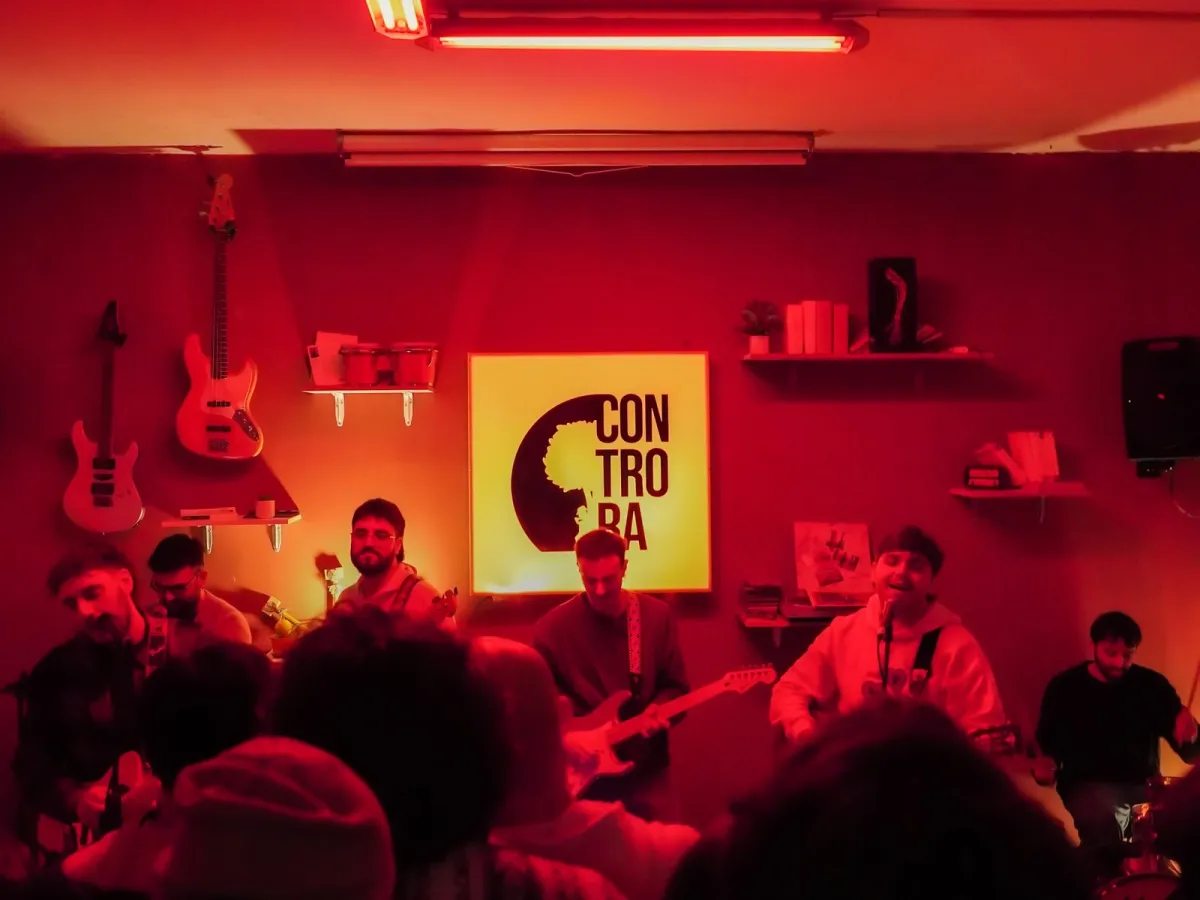 Concerto dal vivo nella sede di Controra ad Angri: band sul palco sotto luci rosse, con il logo Controra alle spalle e il pubblico in primo piano